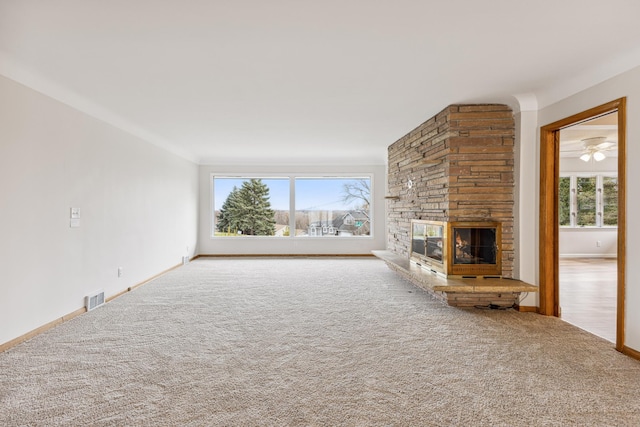 unfurnished living room featuring baseboards, visible vents, carpet flooring, and a stone fireplace