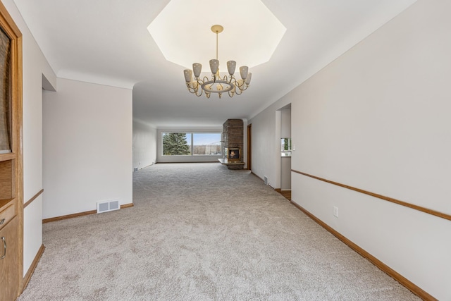 carpeted spare room with a chandelier, a brick fireplace, visible vents, and baseboards