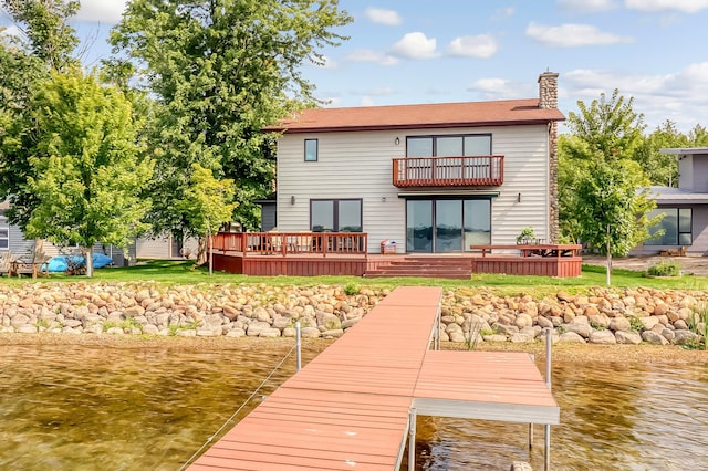 rear view of house with a chimney, a deck with water view, and a balcony