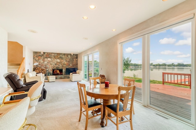 dining area with light carpet, a stone fireplace, a water view, and visible vents