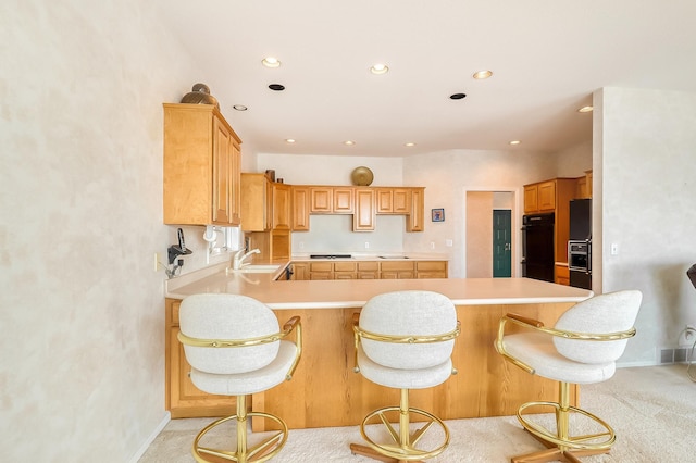 kitchen featuring light carpet, a peninsula, light countertops, black appliances, and a sink