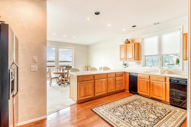 kitchen featuring black dishwasher, a peninsula, light countertops, light wood-style floors, and a sink