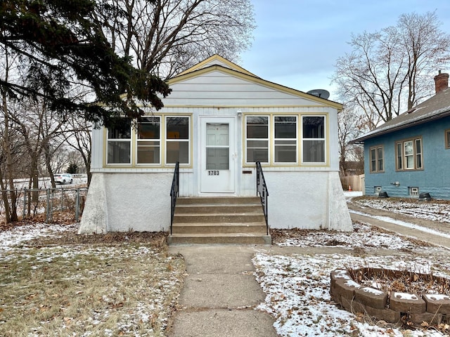 bungalow-style home with entry steps, a fire pit, fence, and stucco siding