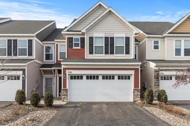 townhome / multi-family property with stone siding, aphalt driveway, an attached garage, and a shingled roof