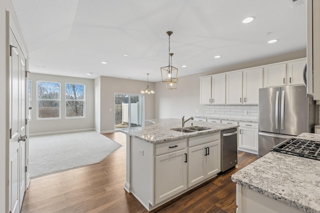 kitchen with a sink, appliances with stainless steel finishes, backsplash, an island with sink, and dark wood finished floors