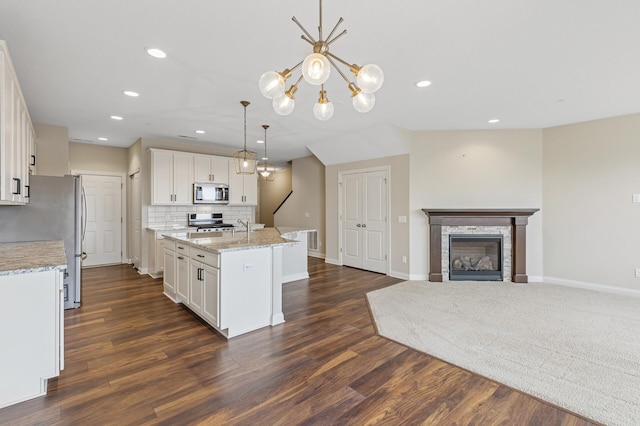 kitchen featuring a center island with sink, white cabinets, decorative backsplash, a glass covered fireplace, and appliances with stainless steel finishes