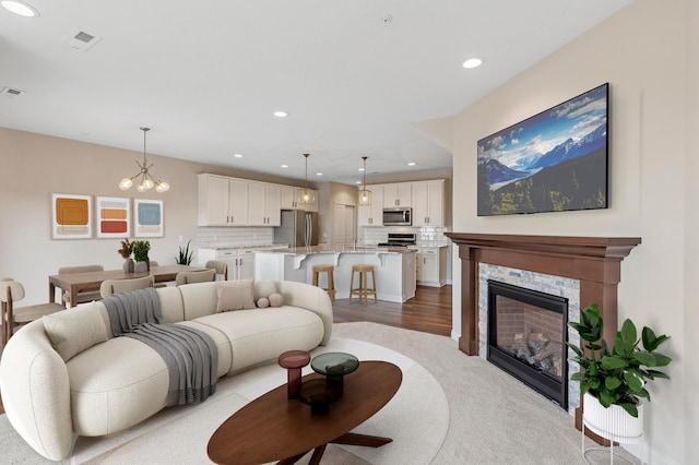 living area with a chandelier, a stone fireplace, visible vents, and recessed lighting