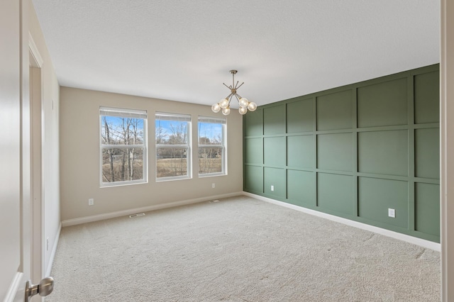 empty room with baseboards, an inviting chandelier, a textured ceiling, carpet floors, and a decorative wall