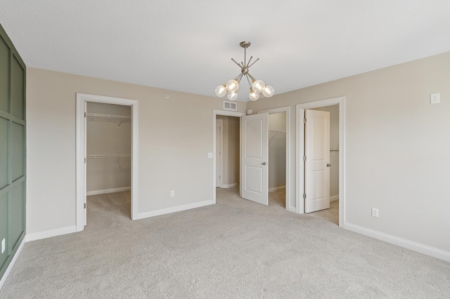 unfurnished bedroom featuring a closet, a walk in closet, visible vents, and light colored carpet