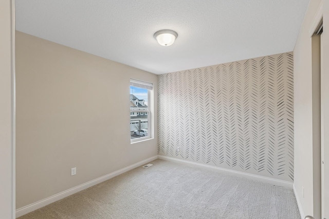 empty room featuring carpet, an accent wall, a textured ceiling, baseboards, and wallpapered walls