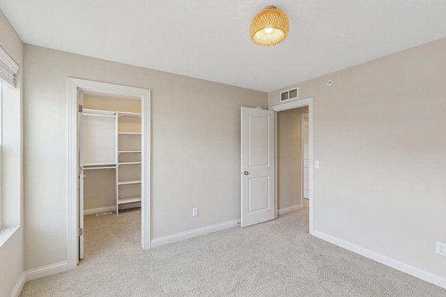 unfurnished bedroom with baseboards, a spacious closet, visible vents, and light colored carpet