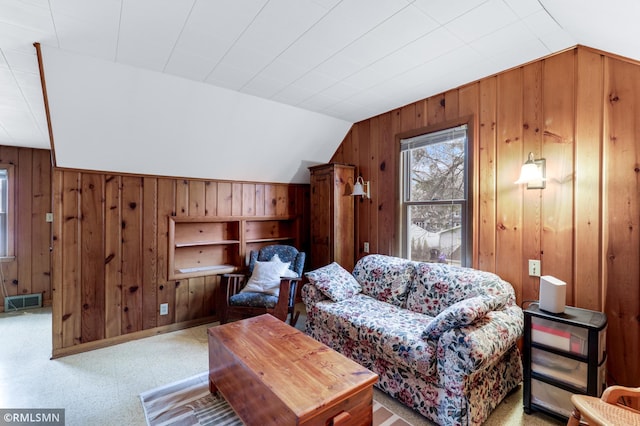 living area with vaulted ceiling, baseboards, visible vents, and wooden walls