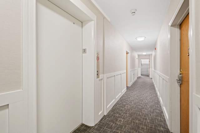 corridor with a wainscoted wall, a decorative wall, and elevator