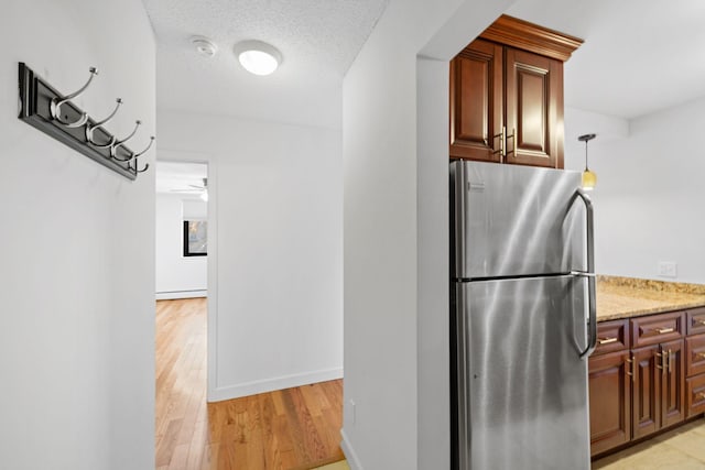 kitchen featuring a textured ceiling, light stone counters, baseboards, light wood-type flooring, and freestanding refrigerator