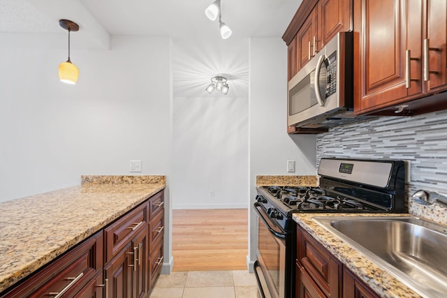 kitchen with a sink, appliances with stainless steel finishes, light stone countertops, tasteful backsplash, and decorative light fixtures