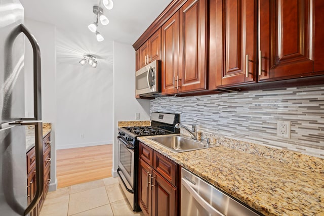 kitchen featuring tasteful backsplash, light stone counters, stainless steel appliances, a sink, and light tile patterned flooring