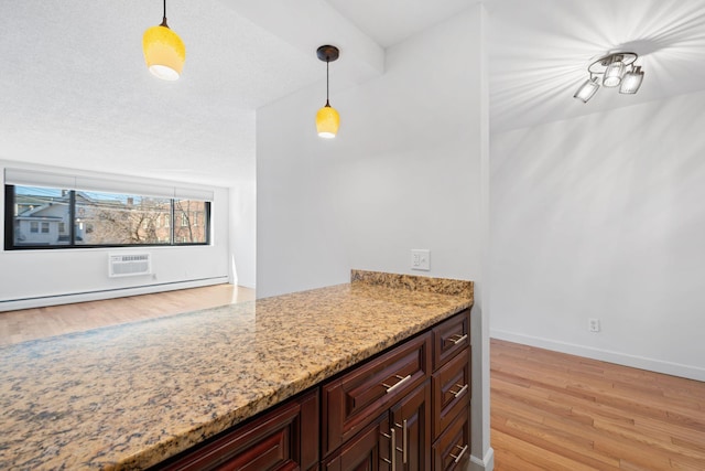 kitchen featuring light wood finished floors, baseboards, decorative light fixtures, light stone countertops, and a textured ceiling