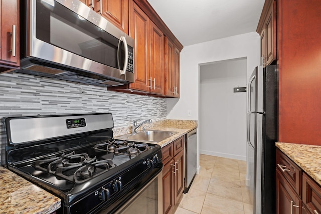 kitchen with light tile patterned floors, a sink, light stone countertops, stainless steel appliances, and backsplash