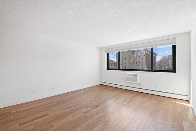 spare room featuring a baseboard heating unit, a wall mounted air conditioner, wood finished floors, and a wealth of natural light