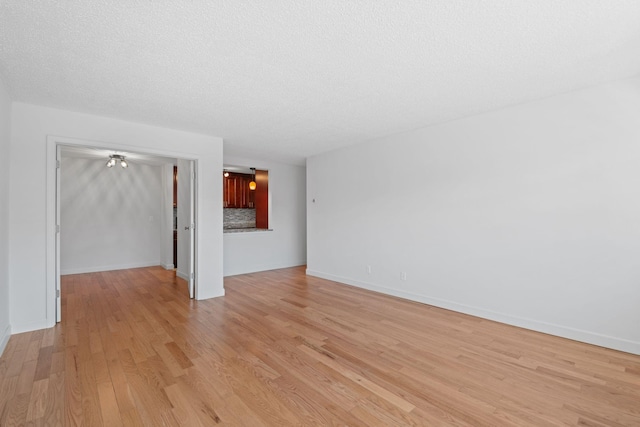 unfurnished living room with light wood-type flooring, baseboards, and a textured ceiling