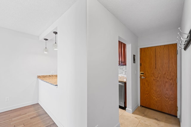 hall featuring a textured ceiling, light wood-style floors, and baseboards