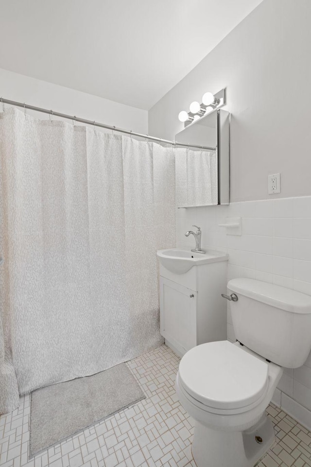 bathroom with wainscoting, toilet, tile patterned floors, vanity, and tile walls