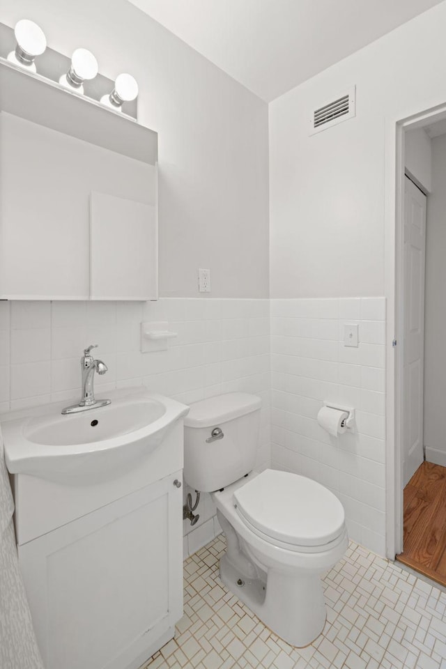 bathroom with visible vents, tile walls, toilet, and vanity