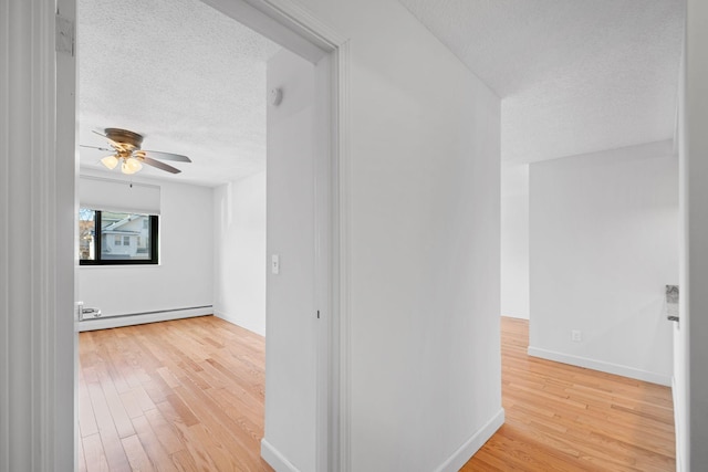 spare room featuring a textured ceiling, baseboard heating, wood finished floors, and a ceiling fan