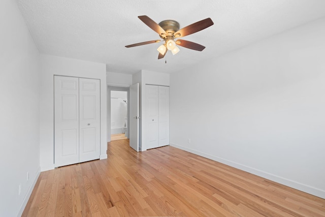 unfurnished bedroom featuring light wood-type flooring, a textured ceiling, baseboards, and multiple closets