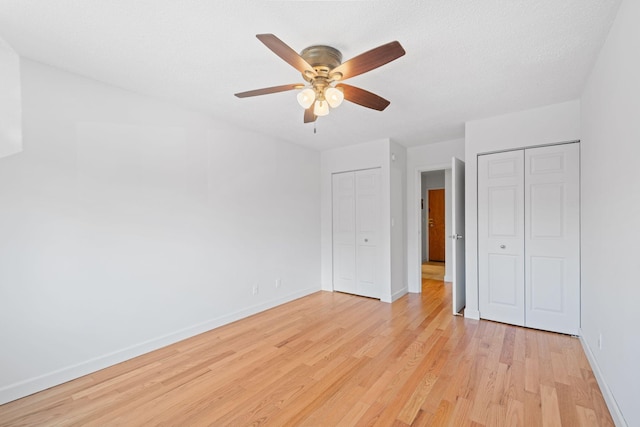 unfurnished bedroom featuring baseboards, light wood-style flooring, ceiling fan, a textured ceiling, and multiple closets