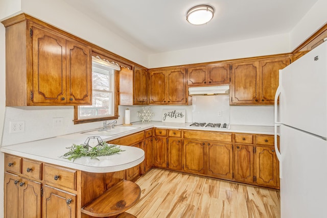 kitchen featuring brown cabinetry, white appliances, a sink, and under cabinet range hood