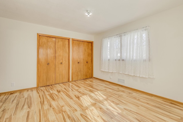 unfurnished bedroom featuring multiple closets, visible vents, baseboards, and wood finished floors