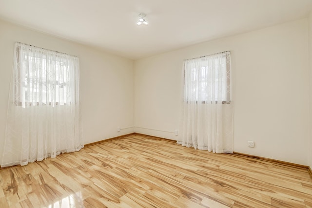 empty room with plenty of natural light, baseboards, and wood finished floors