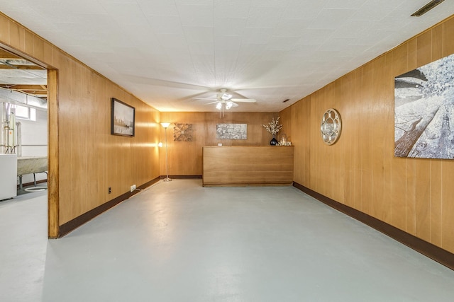 interior space featuring finished concrete flooring, wooden walls, visible vents, baseboards, and ceiling fan