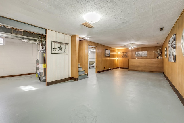 finished basement featuring gas water heater, visible vents, stairway, wooden walls, and baseboards