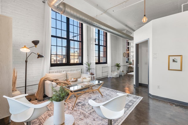 living area featuring concrete flooring, brick wall, a high ceiling, and baseboards