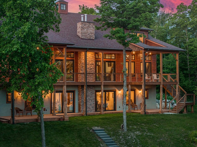 back of house with stone siding, a yard, a patio, and stairway