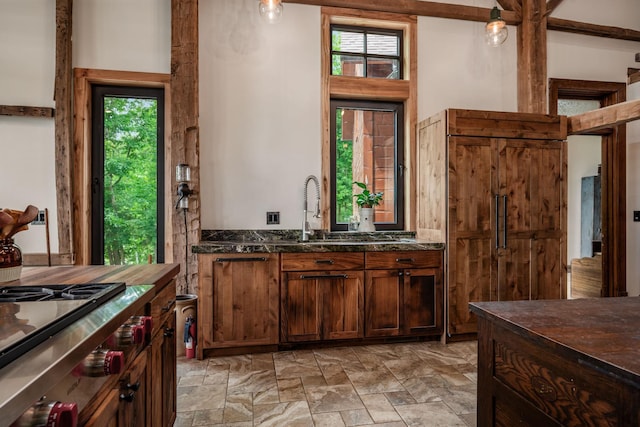 kitchen with dark stone counters, stone finish floor, stainless steel gas stovetop, and a sink