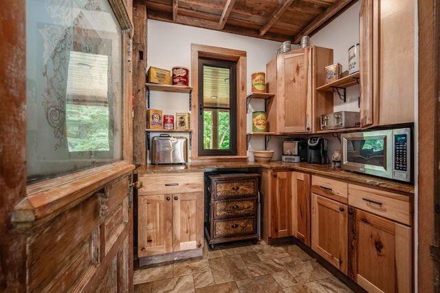 kitchen featuring open shelves, stainless steel microwave, stone finish floor, dark stone countertops, and wooden ceiling