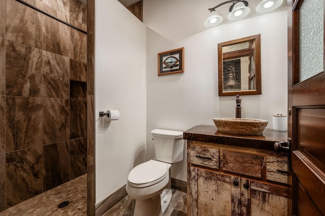 bathroom featuring tiled shower, vanity, toilet, and baseboards