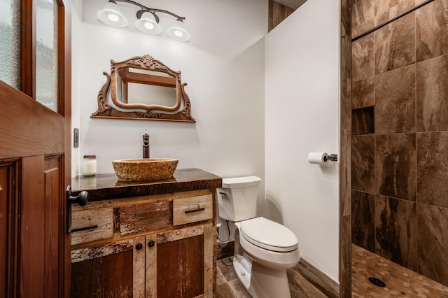 full bathroom featuring toilet, a tile shower, and vanity