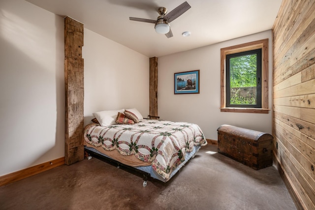 bedroom with concrete flooring, wood walls, a ceiling fan, and baseboards