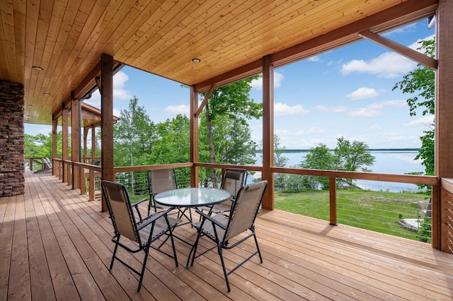 wooden deck with outdoor dining area, a water view, and a lawn