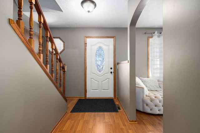 foyer entrance featuring stairway, wood finished floors, visible vents, baseboards, and arched walkways