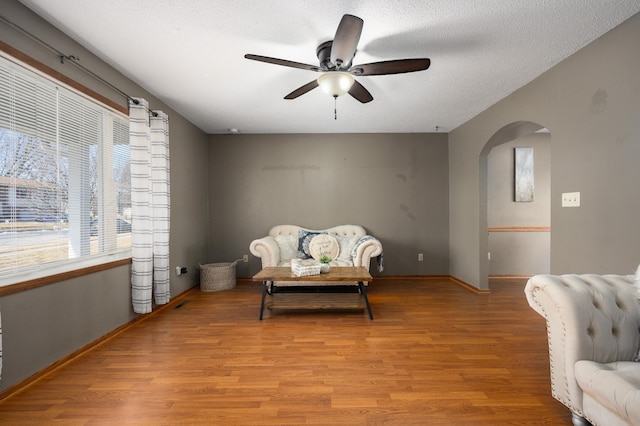 sitting room featuring light wood-type flooring, a ceiling fan, a textured ceiling, arched walkways, and baseboards