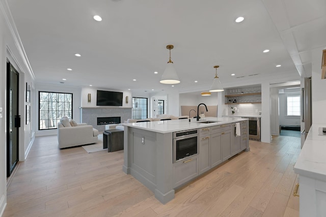 kitchen with beverage cooler, ornamental molding, gray cabinets, a fireplace, and stainless steel oven