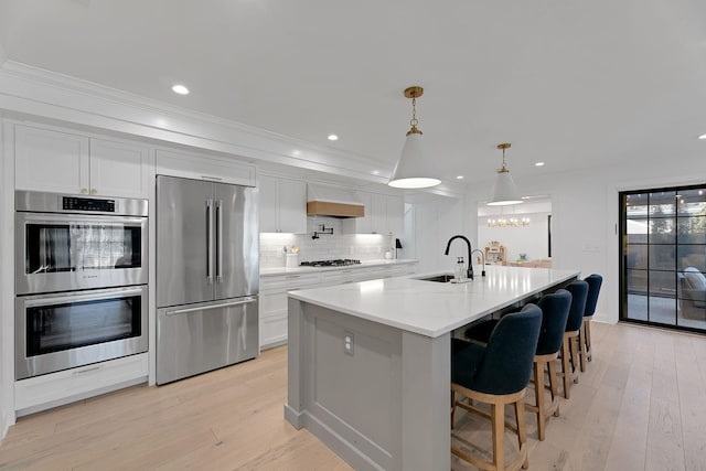 kitchen with white cabinets, decorative backsplash, appliances with stainless steel finishes, light wood-type flooring, and a sink