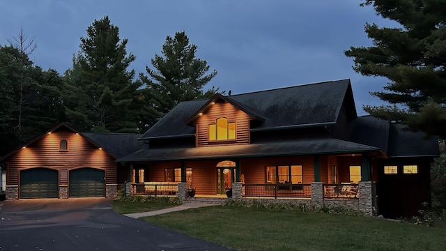 view of front facade with a front lawn, a garage, covered porch, and stone siding