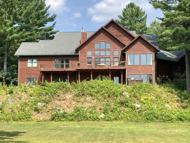 back of property featuring a lawn, a chimney, and a wooden deck