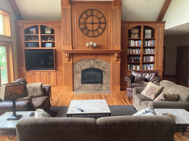 living room featuring lofted ceiling, built in features, a tiled fireplace, and wood finished floors